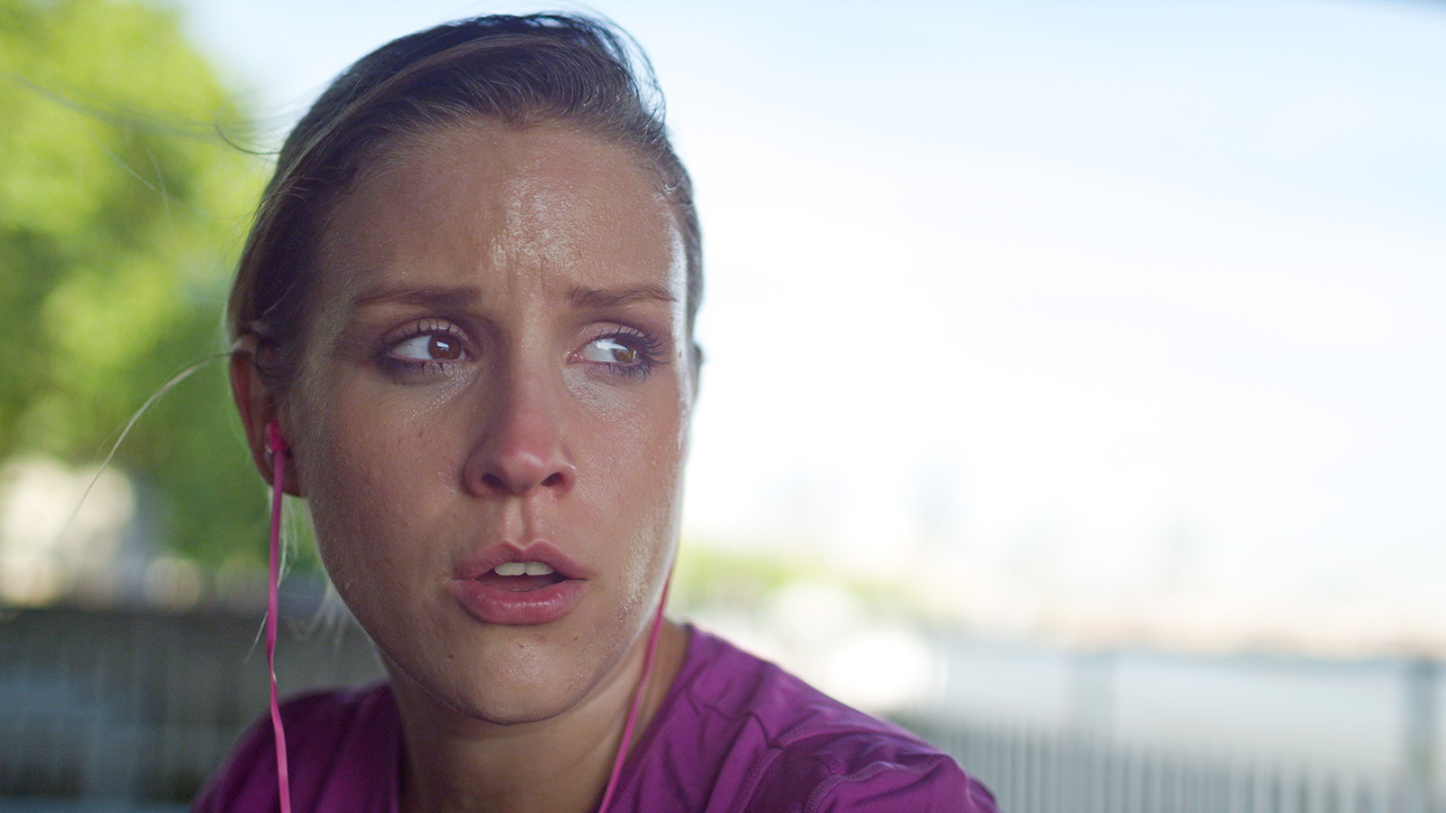 A woman's face, sweating, taking a break after a jog.
