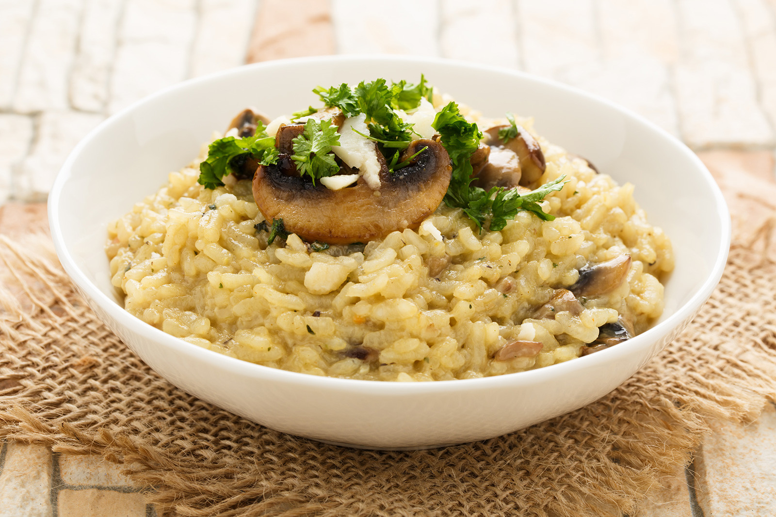 Mushroom risotto with fresh herbs, Parmesan cheese and a bunch of mushrooms on top of it, in a white bowl.