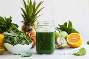 healthy green smoothie with spirulina in front of fresh fruits and vegetables