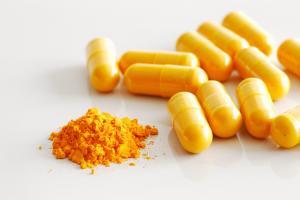 group of turmeric supplement caps beside turmeric powder