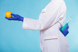 woman in lab coat holding syringe and apple