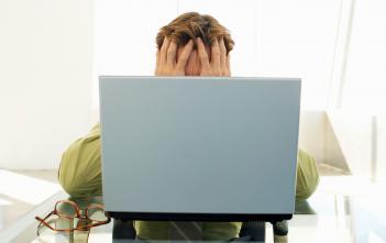 anxious man covering face while sitting before a laptop